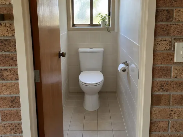 Clean white toilet in a tiled small bathroom with a window and brick doorway in Gymea