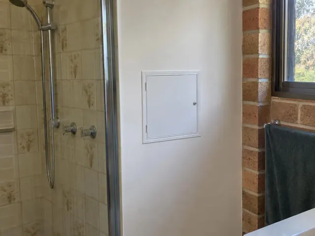 Small white access panel on a painted bathroom wall beside a shower and brick window alcove in Gymea Bay